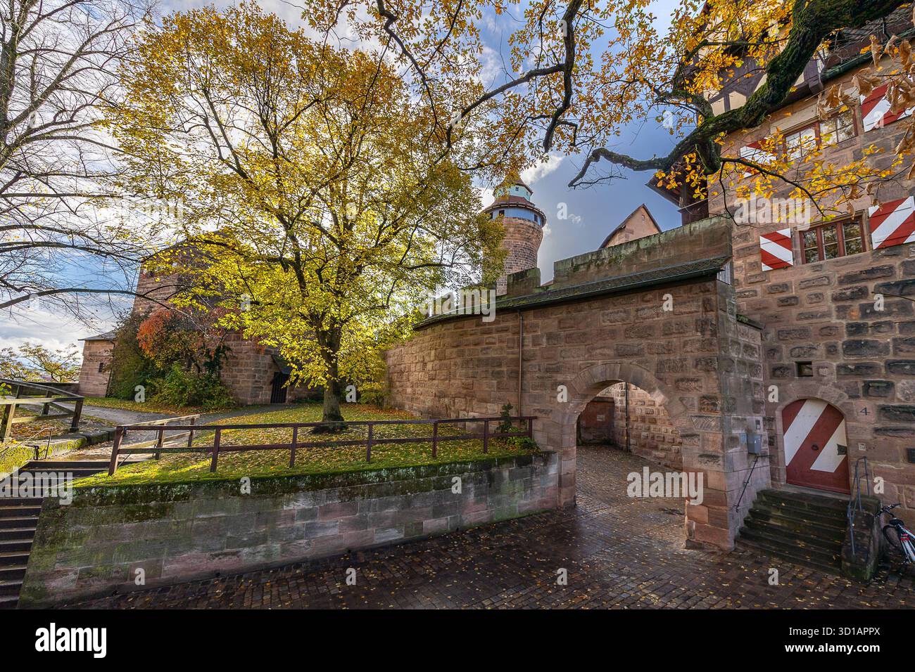 Herbstliches Wechselwetter, Nürnberg, 27.10.2025 Herbstliche Ansicht im Innenbereich der Kaiserburg in Nürnberg, Bayern, Deutschland. Im Zentrum des Bilds erhebt sich der runde Sinwellturm mit seiner markanten Kuppel. Rechts im Bild ist ein historischer Torbogen aus Sandstein mit rot-weiß gestrichenen Fensterläden zu sehen. Links führen Stufen und ein Weg auf das Burgplateau. Das herabgefallene Laub, die belaubten Bäume und die nassen Pflastersteine deuten auf kürzliches Regenwetter hin. Die Szene ist von spätherbstlicher Stimmung und zeigt den Erhaltungszustand der mittelalterlichen Burganla Stockfoto