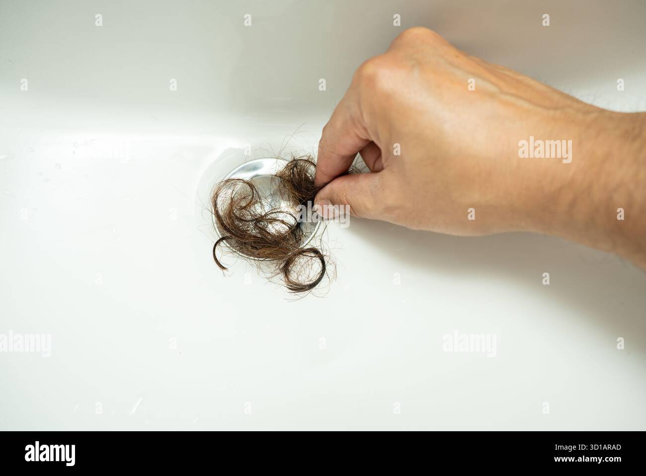 Der Abfluss im Bad war verstopft mit Haarklumpen und Dreck. Die Hand des Mannes zieht Haare aus dem Abfluss im Bad Stockfoto
