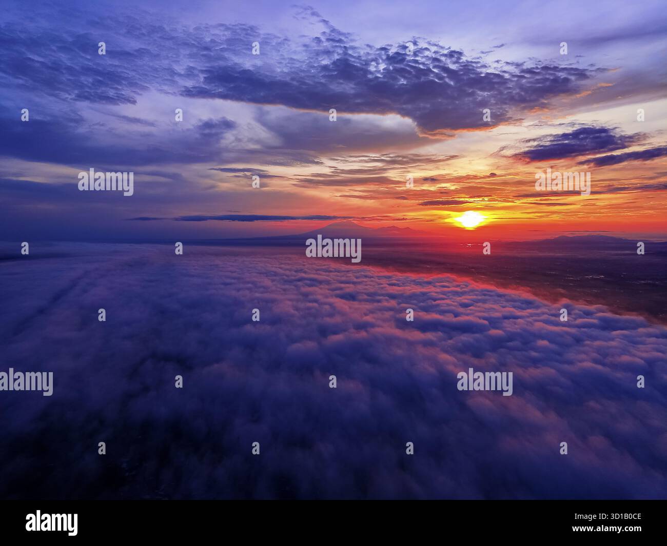 Aus der Vogelperspektive auf einen atemberaubenden Sonnenaufgang über einer dicken Wolkendecke, mit dem strahlenden Licht der Sonne im Kontrast zur fernen Silhouette des Lawu Mountain, Karanganyar, Zentral-Java, Indonesien. Stockfoto