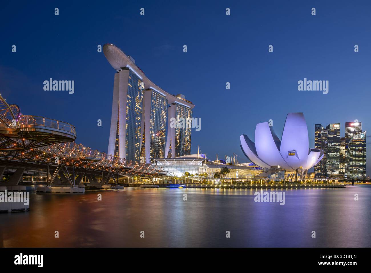 Blick auf die beleuchtete Helix Bridge, die sich im Wasser spiegelt und zum berühmten Marina Bay Sands und ArtScience Museum unter einem dunkelblauen Himmel führt, Singap Stockfoto