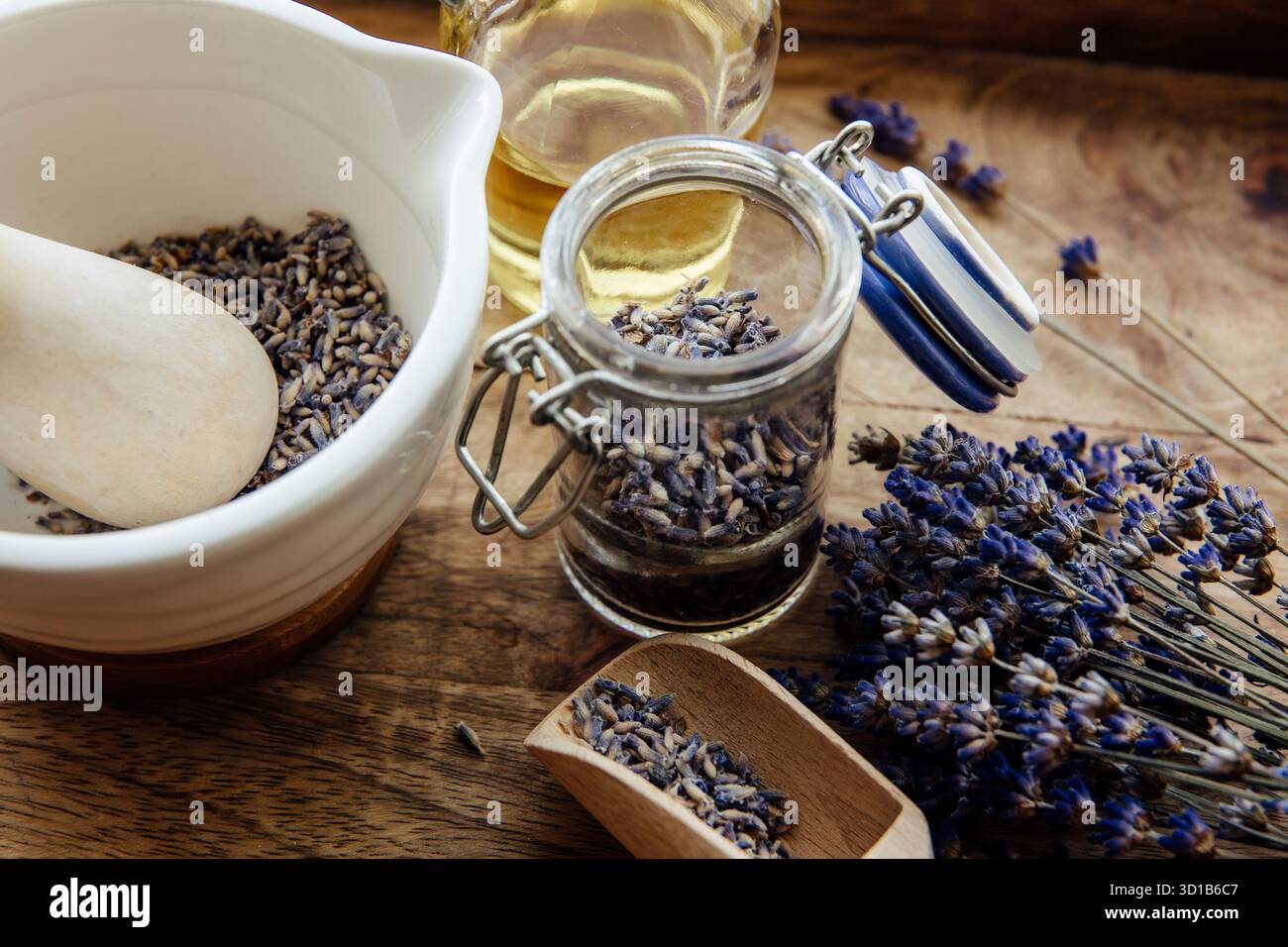 Getrocknete Lavendelblüten im Klarglas, mit Mörtel und Pistill gefüllt mit Blumen und Blumenstrauß daneben. Brauner Holzhintergrund. Stockfoto
