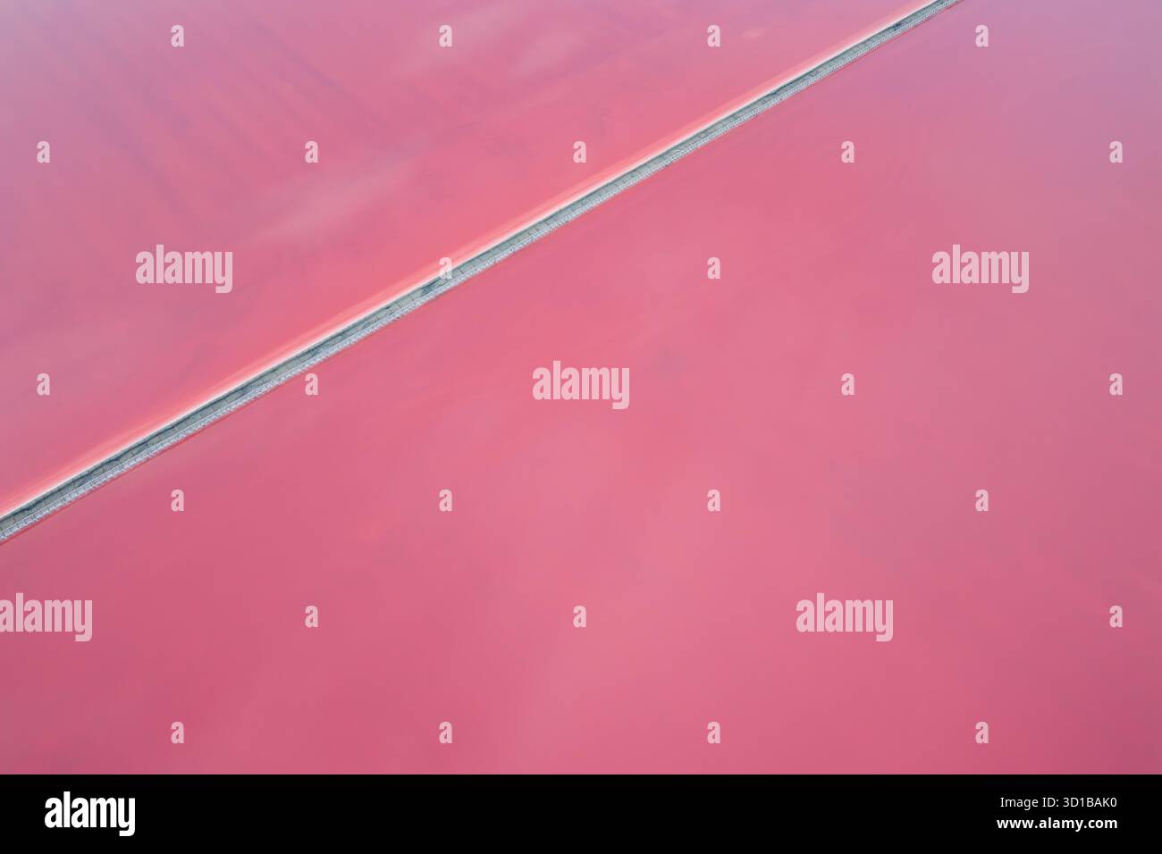 Aus der Vogelperspektive pulsierende rosafarbene Salzebenen, die durch einen schmalen Streifen getrennt sind und eine beeindruckende geometrische Landschaft schaffen, Aigues, Occitanie, Frankreich. Stockfoto