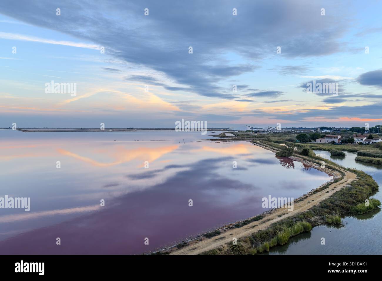 Aus der Vogelperspektive das rosa Wasser reflektiert den pastellfarbenen Himmel, geteilt durch einen schmalen Landstreifen, der zur Stadt führt, Aigues, Occitanie, Frankreich. Stockfoto