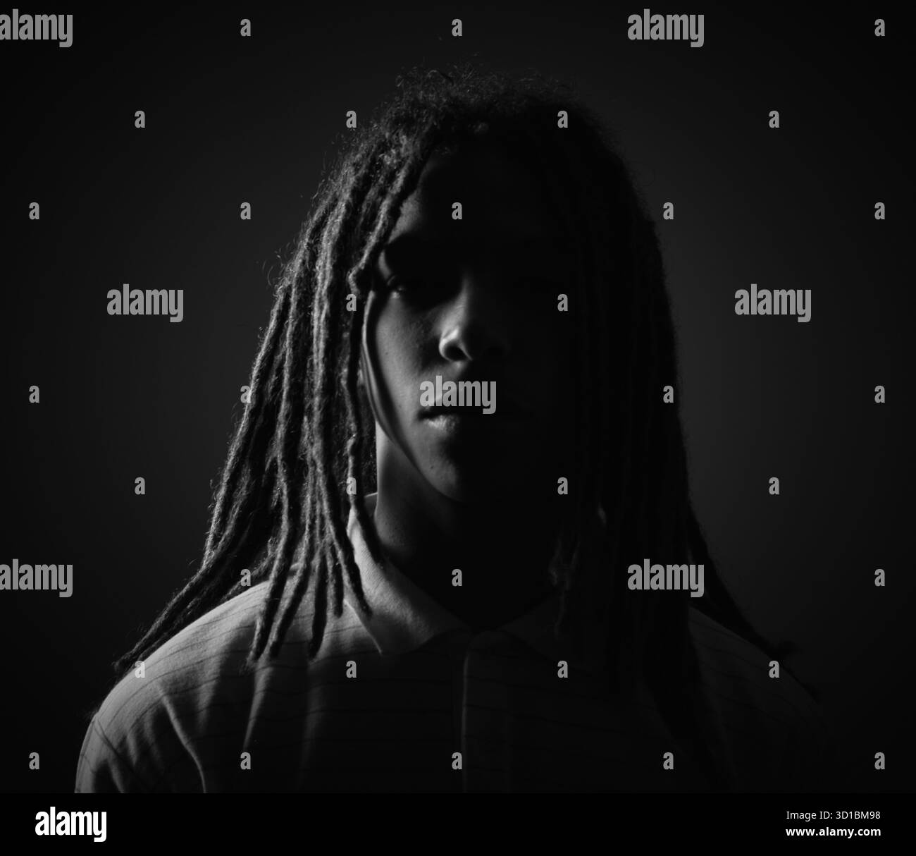 Ein Mann mit Dreadlocks, der bei schlechtem Licht steht und eine mysteriöse und ernste Stimmung erzeugt Stockfoto