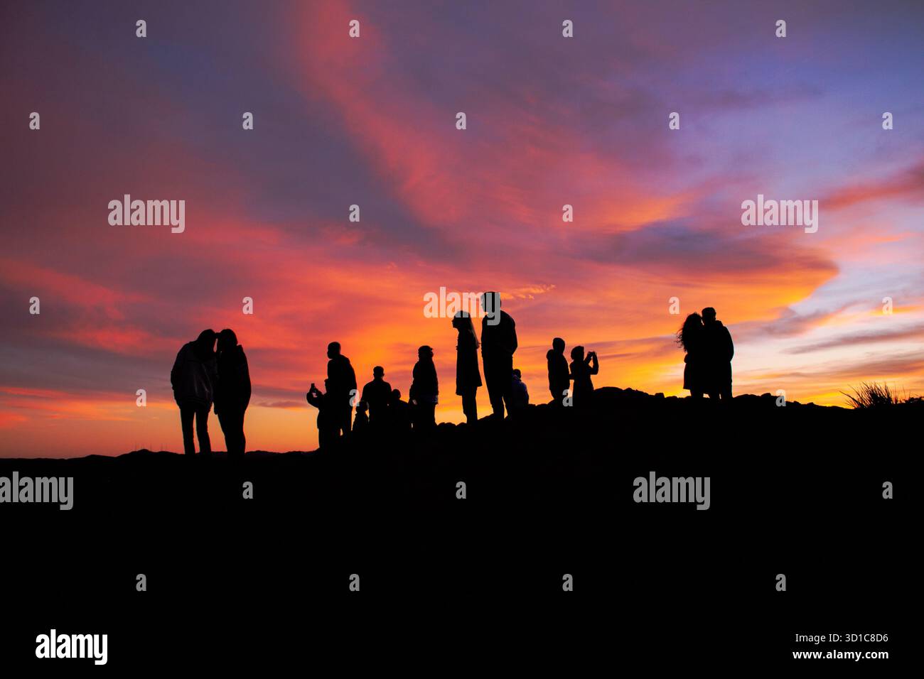 Eine Gruppe von Personen mit Silhouette versammelte sich auf einem Hügel während eines lebendigen Sonnenuntergangs mit rosa, orange und violetten Wolken, einer warmen und dramatischen Abendatmosphäre Stockfoto