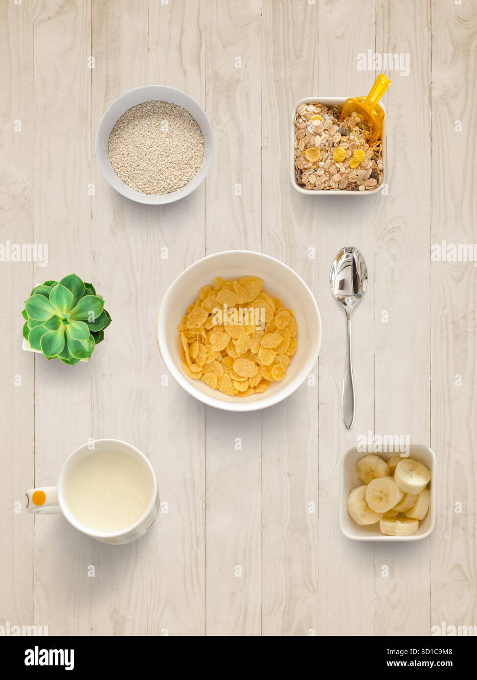 Blick von oben auf Müsli, Banane, Milch, Hafer und Müslischalen auf dem Holztisch, die eine gesunde Zubereitung des Frühstücks darstellen Stockfoto