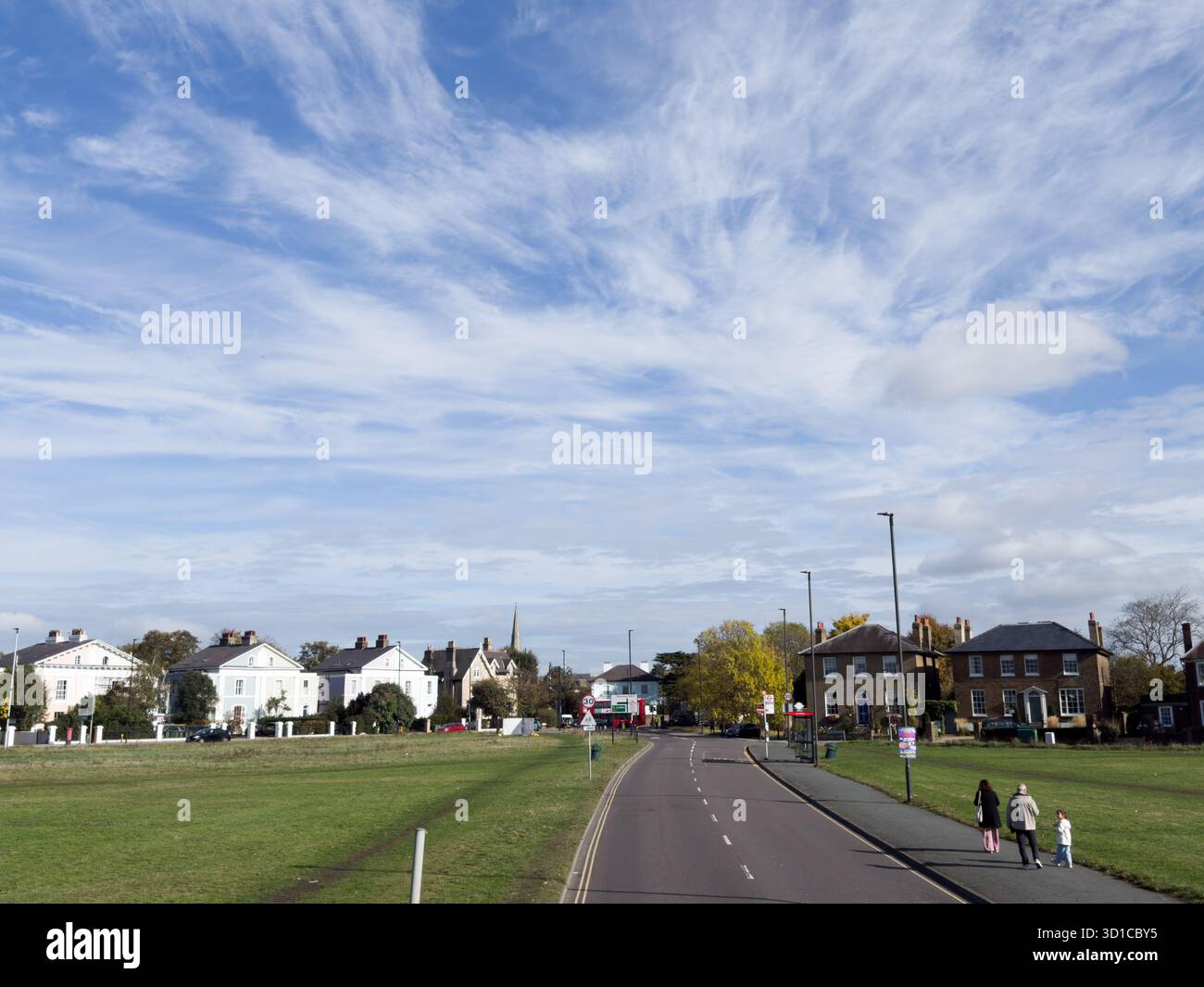 Fußgänger, die entlang der Straße neben Blackheath Common unter einem blauen Himmel mit sich bewegenden weißen Wolken und einer Reihe von Doppelhäusern im Backgro spazieren Stockfoto