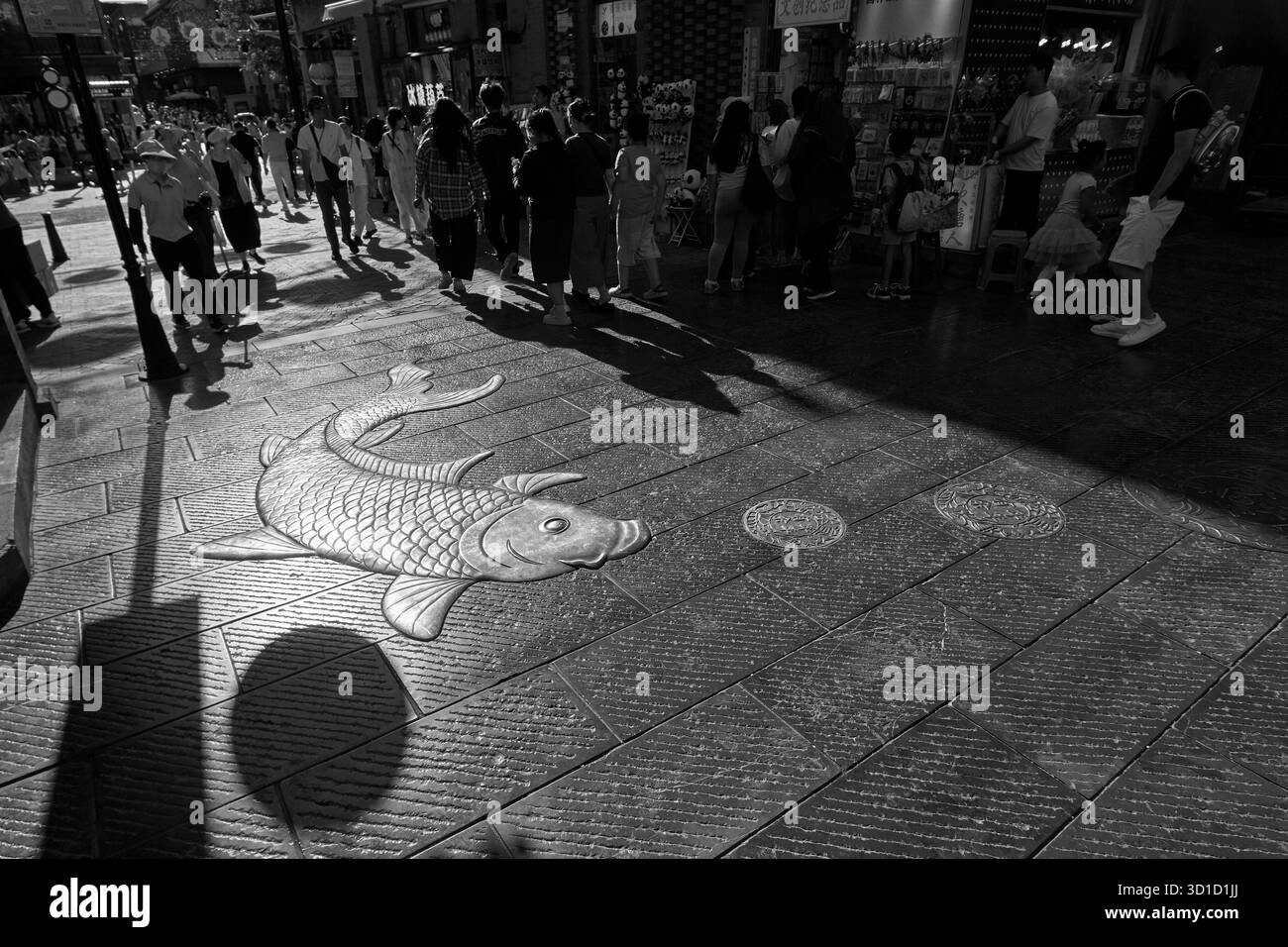 Schwarz-weiße Straßenszene mit goldenem Karpfen auf dem Bürgersteig im angesagten Viertel Dashilan Hutong in der Nähe der Qianmen Straße in Peking Stockfoto