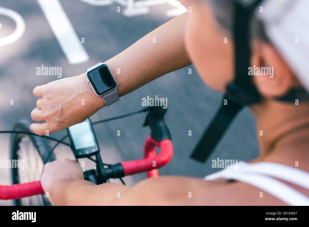 Nahaufnahme einer Radfahrerin, die Smartwatch während der Fahrt im Freien auf markiertem Radweg benutzt Stockfoto