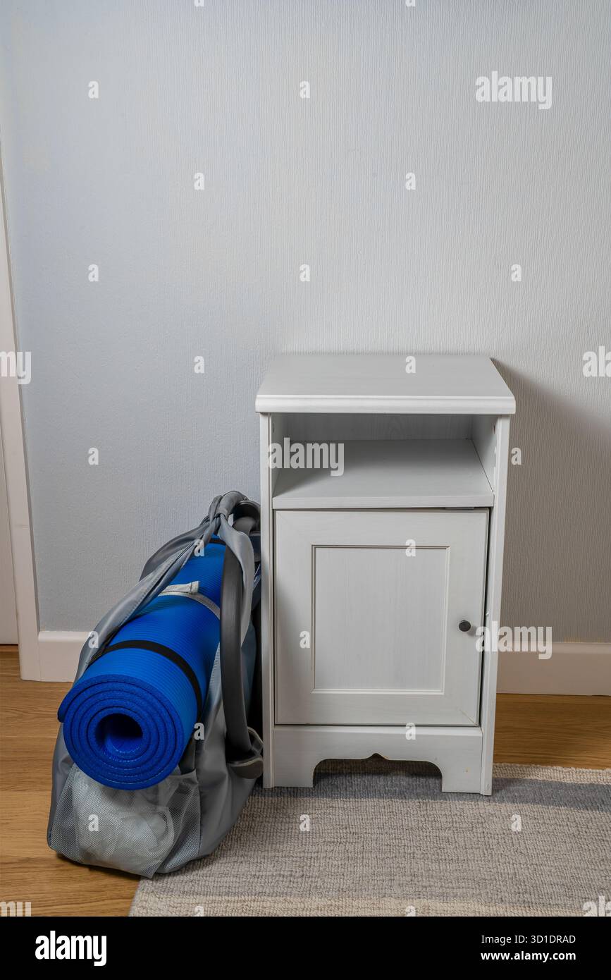 Weißer Schrank im Flur des Hauses mit einem Pilates Übungsbeutel mit einer gerollten blauen Matte daneben, Gesundheit und Fitness bezogen Bild Stockfoto