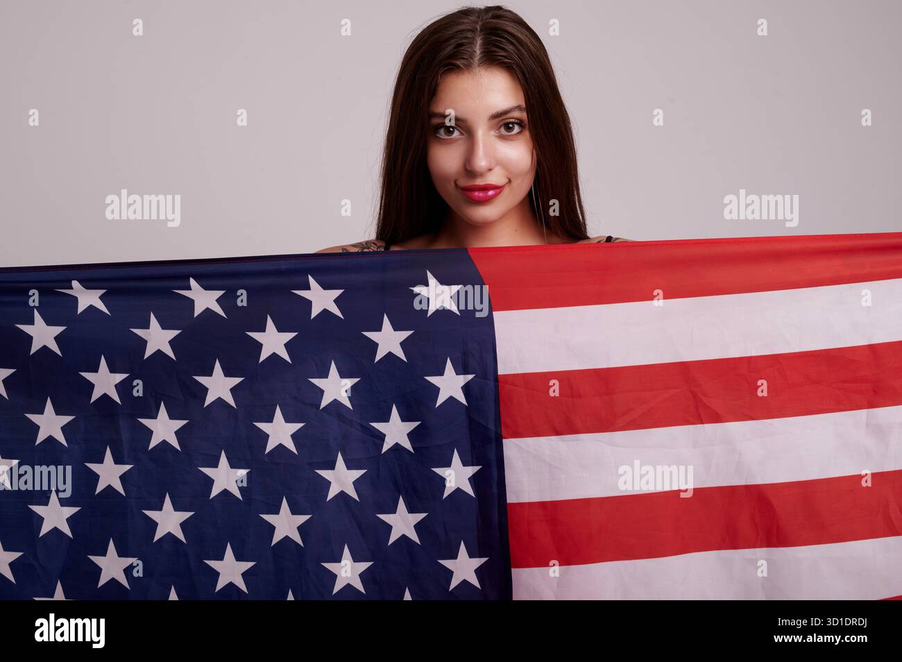 Freundliches Studio-Porträt mit einer jungen Frau, die über die US-Flagge blickt. Warmes, ansprechbares Bild für Community-Veranstaltungen, Schulprojekte und ho Stockfoto