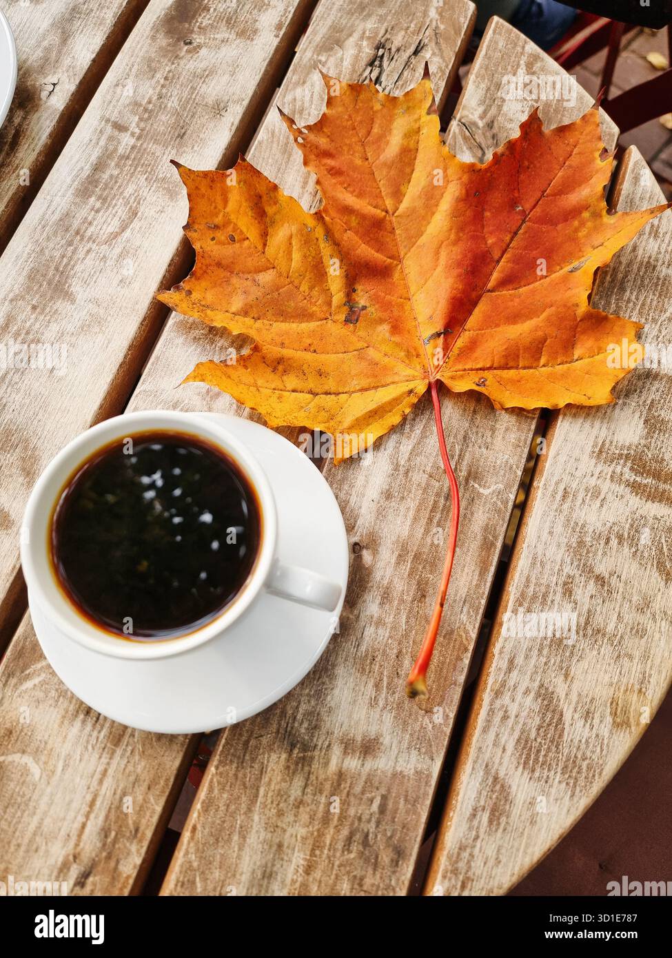 Tasse Kaffee und Herbstahornblatt. (Vertikales Bild) kleine Tasse Kaffee auf einem Holzlattentisch, großes orangefarbenes Ahornblatt. Stockfoto
