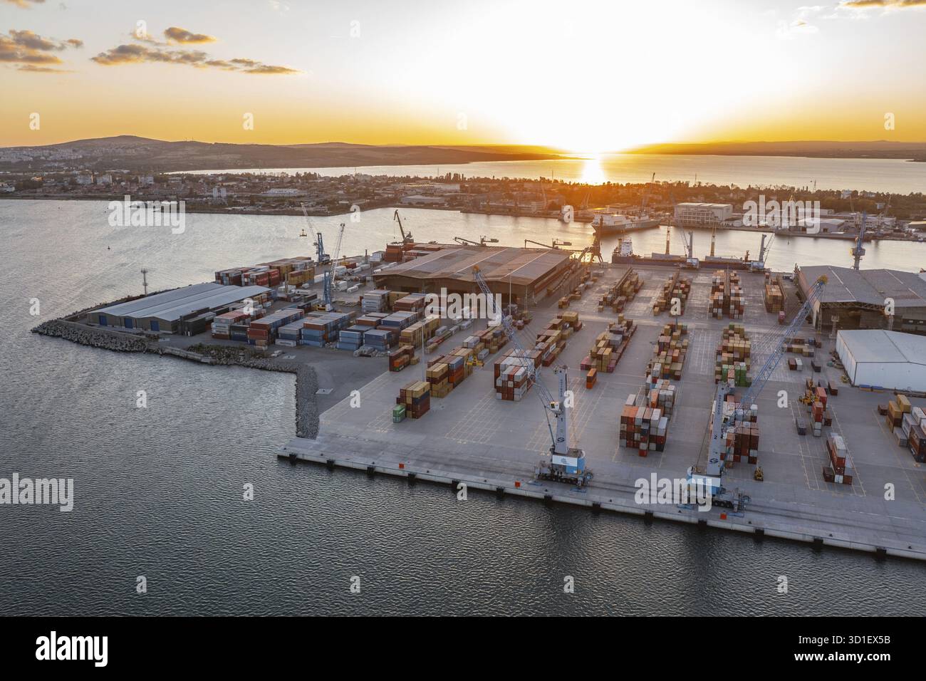 Luftaufnahme eines Frachthafens mit Kränen und Containern bei Sonnenuntergang. Luftaufnahme zum neuen Containerentladeterminal des Hafens von Burgas, Bulgarien bei Sonnenuntergang Stockfoto