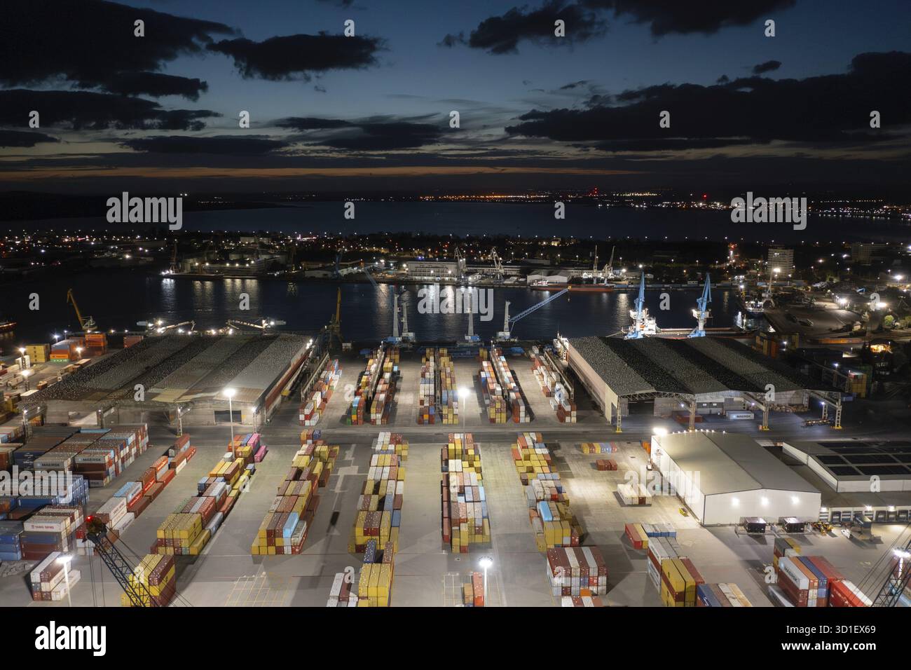 Nachtansicht auf einen belebten Hafen mit beleuchteten Containern und Kränen am Ufer. Aus der Vogelperspektive zu einem Container-Entladeterminal des Hafens von Burga Stockfoto