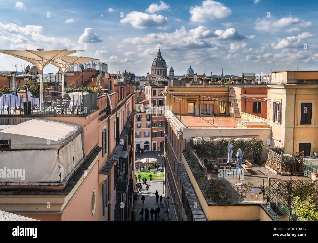 Sonnendurchflutete Dachterrasse in Rom mit pastellfarbenen Gebäuden, Sonnenschirmen und einer Stadtstraße darunter. Lebhafte urbane Stimmung mit kuppelförmigen Silhouetten und blauen s Stockfoto