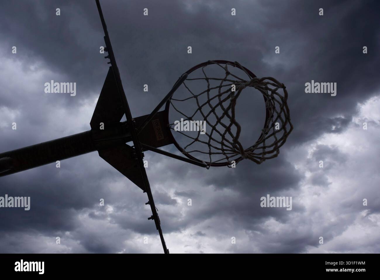 Basketballkorb vor dunklem, bewölktem Himmel, symbolisiert stürmisches Wetter und Outdoor-Sport Stockfoto