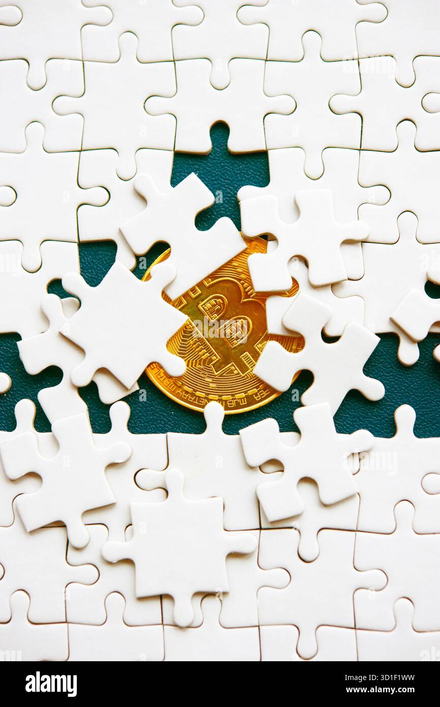 Goldene Bitcoin-Münze versteckt unter Puzzleteilen, die Geheimnis und Komplexität in Kryptowährung darstellen Stockfoto