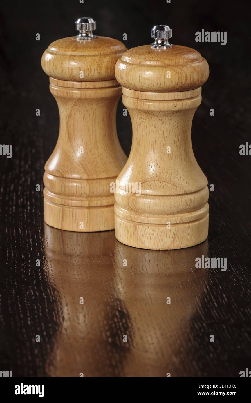 Zwei hölzerne Pfeffermühlen auf dunkler Tischoberfläche Stockfoto