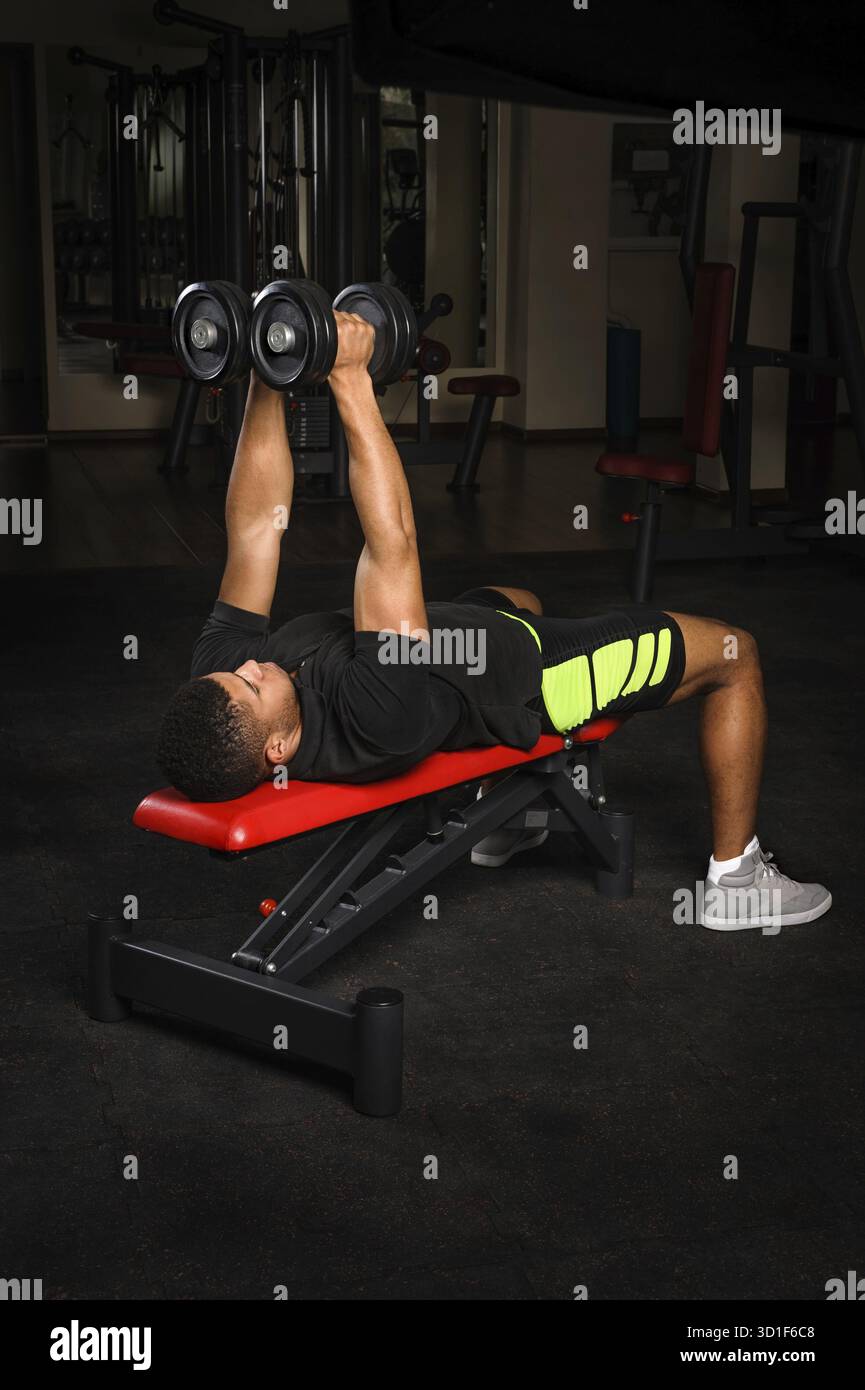 Hübscher junger afrikanischer Abstammung Mixed-Race-Mann, der im Fitnessstudio Armbank Fliegen mit Kurzhanteln macht Stockfoto