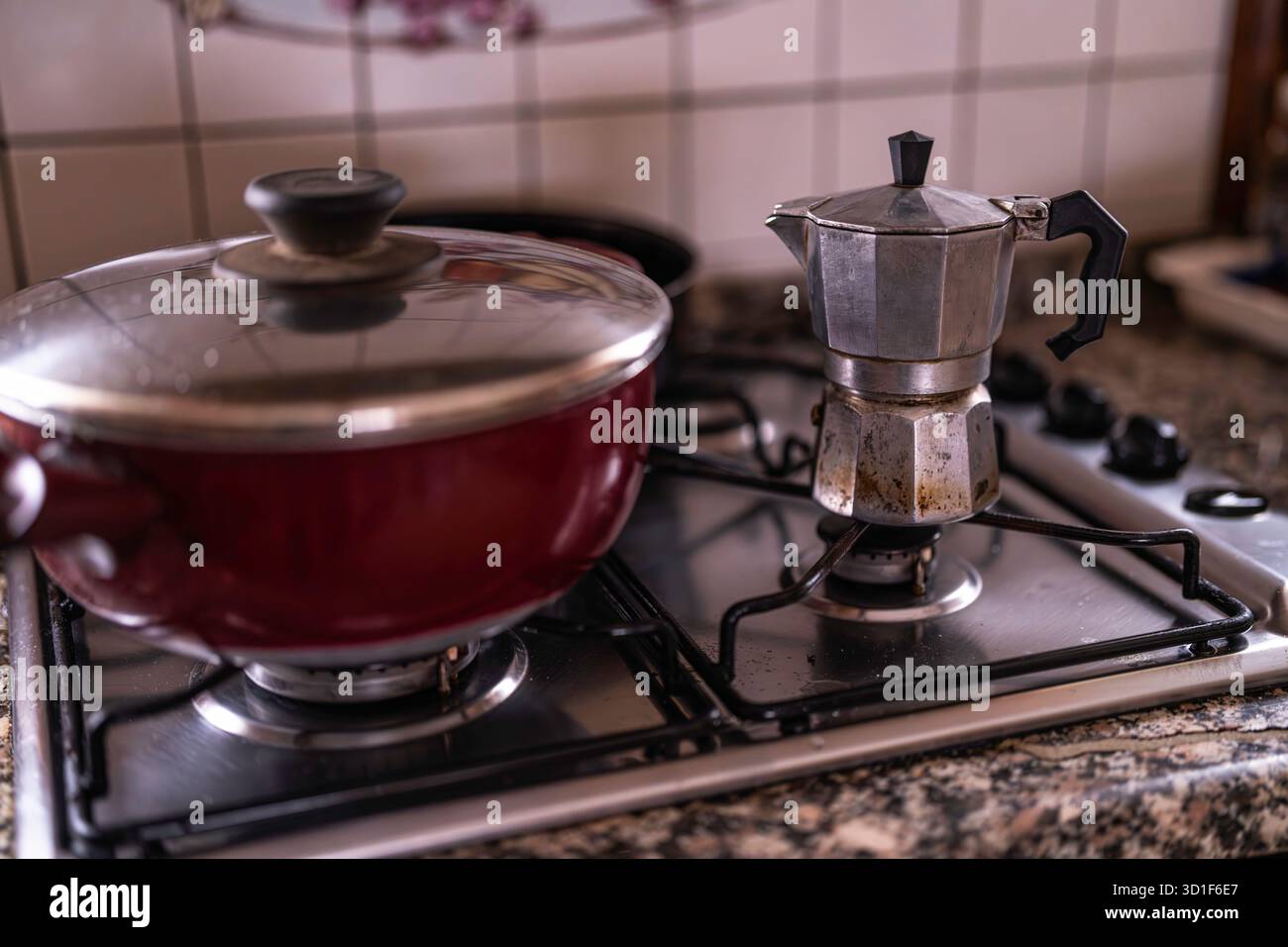 Traditioneller Mokakopf neben einem roten Kochtopf auf einem Gasherd über Granitarbeitsfläche, Dampf steigt, wenn Frühstück Kaffee und Morgenmahl zubereitet werden Stockfoto