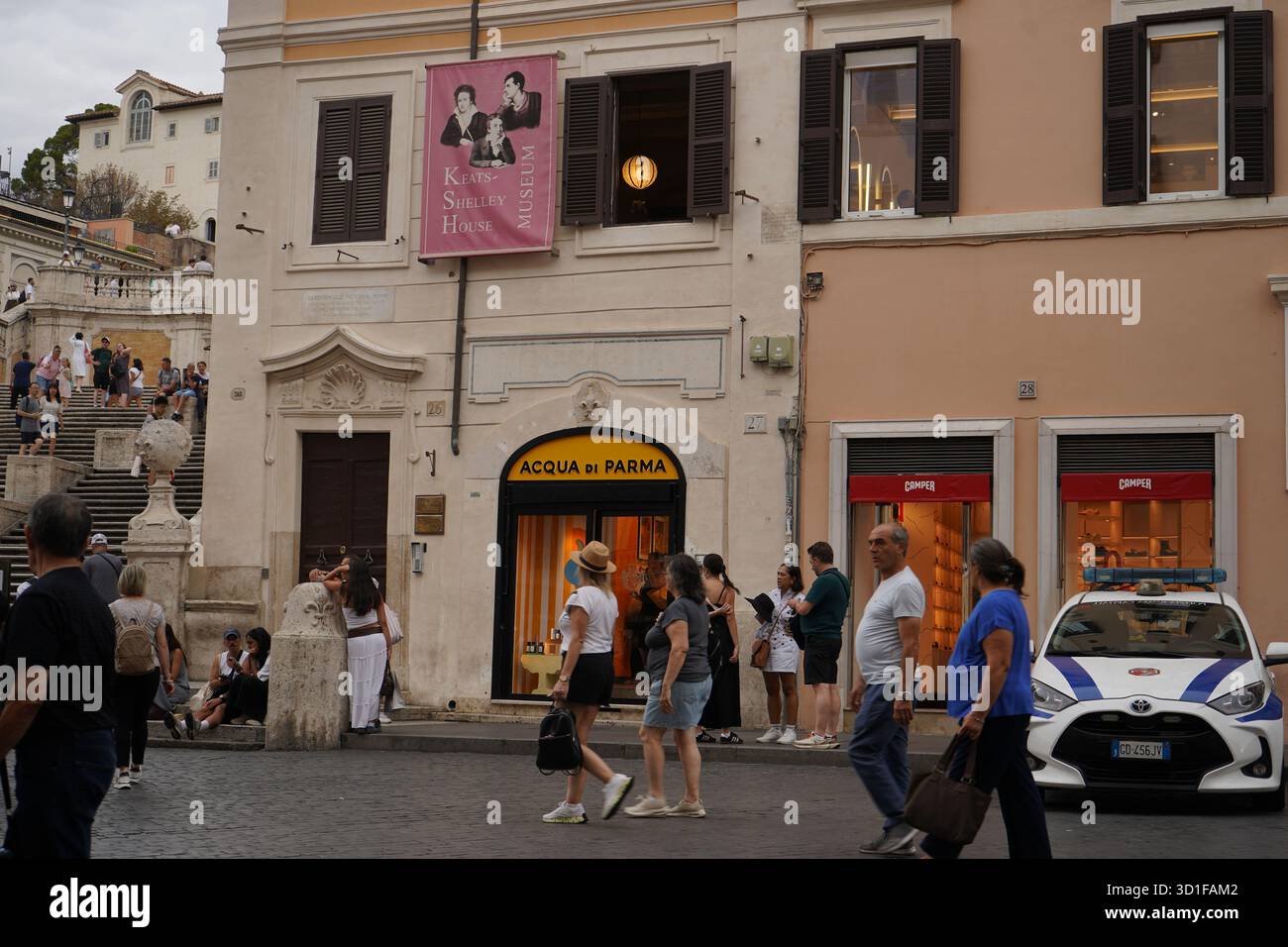 Touristen spazieren vorbei am historischen Keats-Shelley House Museum und der luxuriösen Boutique Acqua di Parma in der Nähe der Spanischen Treppe, mit einem Polizeiauto vor der Tür. Stockfoto