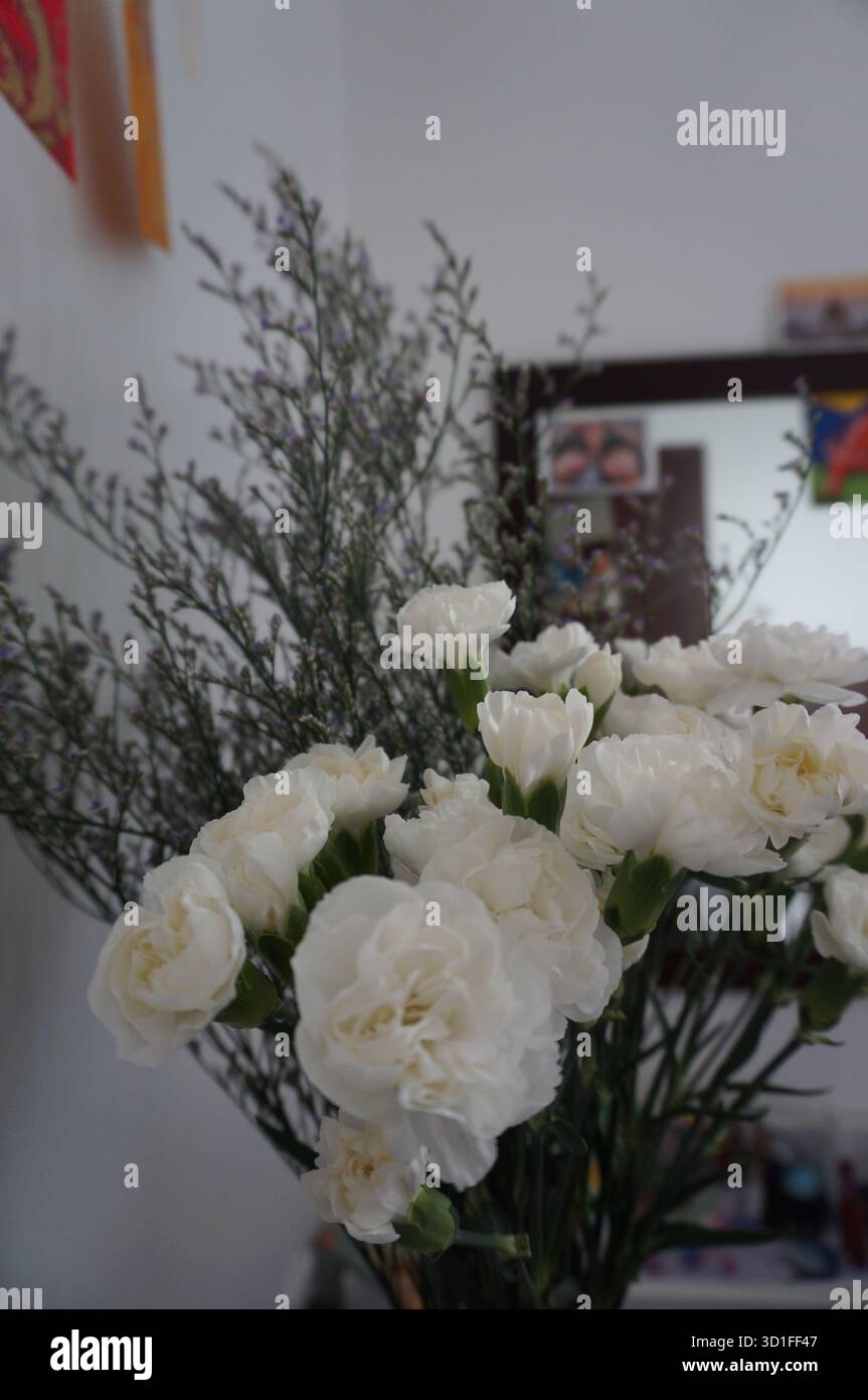 Ein zarter Blumenstrauß aus weißen Nelken in einer Glasvase auf einem Holztisch vor neutralem Hintergrund. Stockfoto