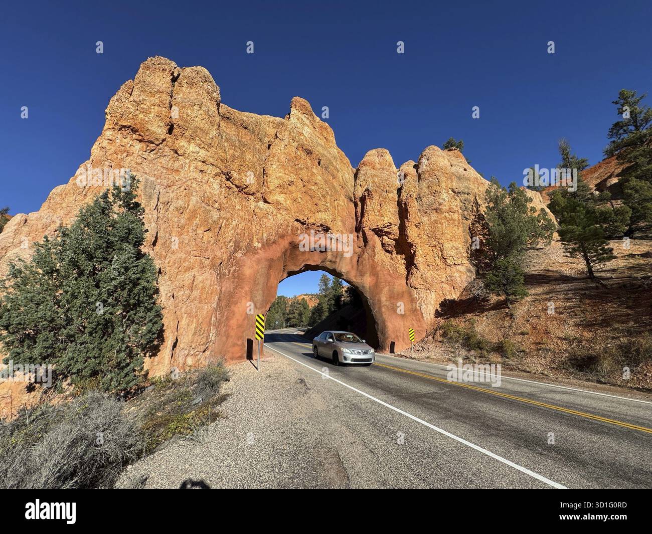 Der Bryce Canyon National Park befindet sich im Südwesten von Utah, einem roten Sandsteinbogen über einer Straße in einer Wüstenlandschaft mit klarem blauem Himmel und einem vorbeifahrenden Auto Stockfoto