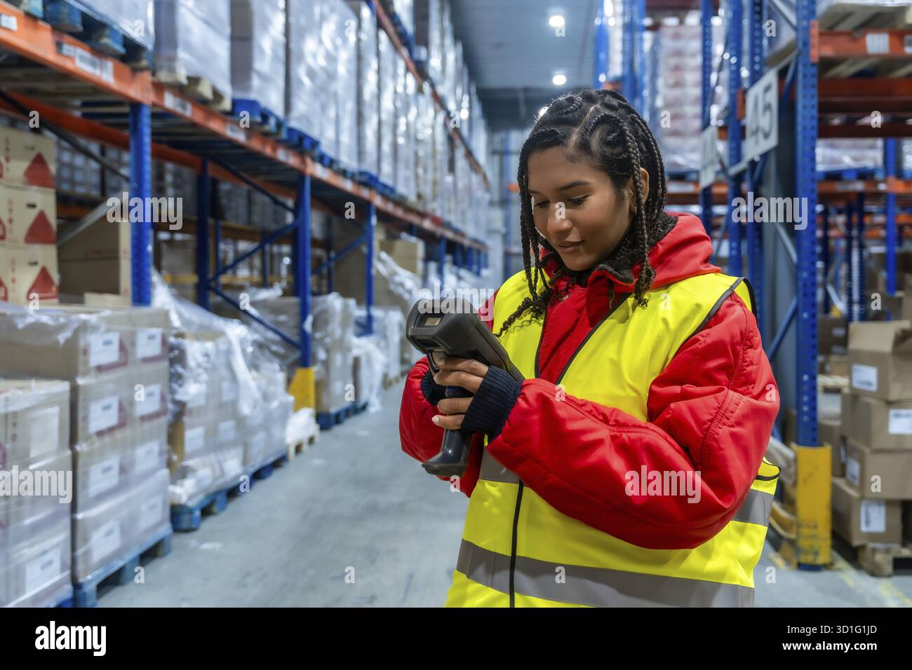 Logistikmitarbeiter tragen warme Kleidung und eine Sicherheitsweste, die mit einem Handscanner in hohen Regalen mit verpackten Regalen die Inventarkontrolle durchführt Stockfoto