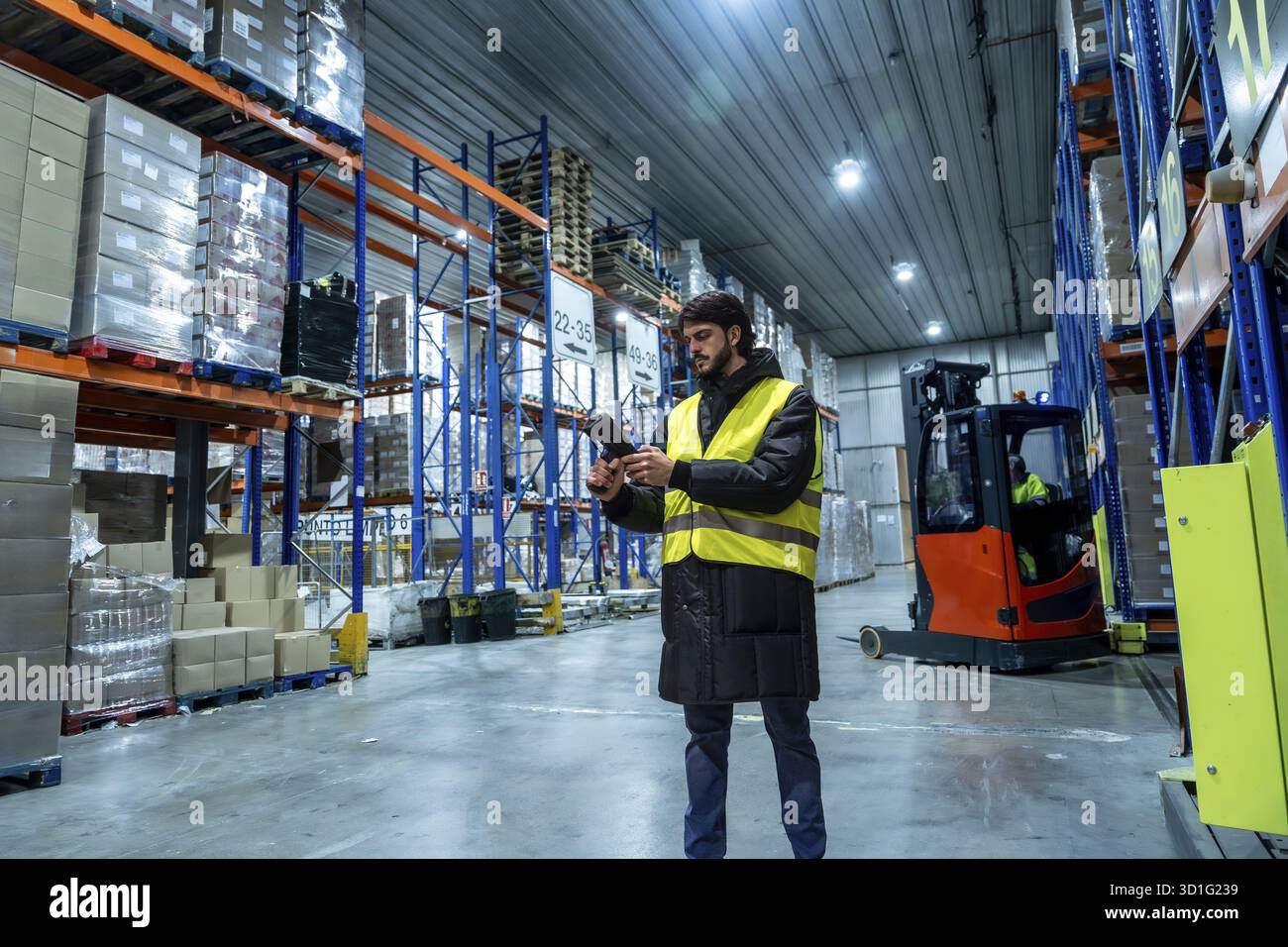 Logistikmitarbeiter tragen Schutzkleidung, scannen Produkte mit einem Handscanner in einem modernen Kühllager mit hohen Regalen, implementieren Stockfoto