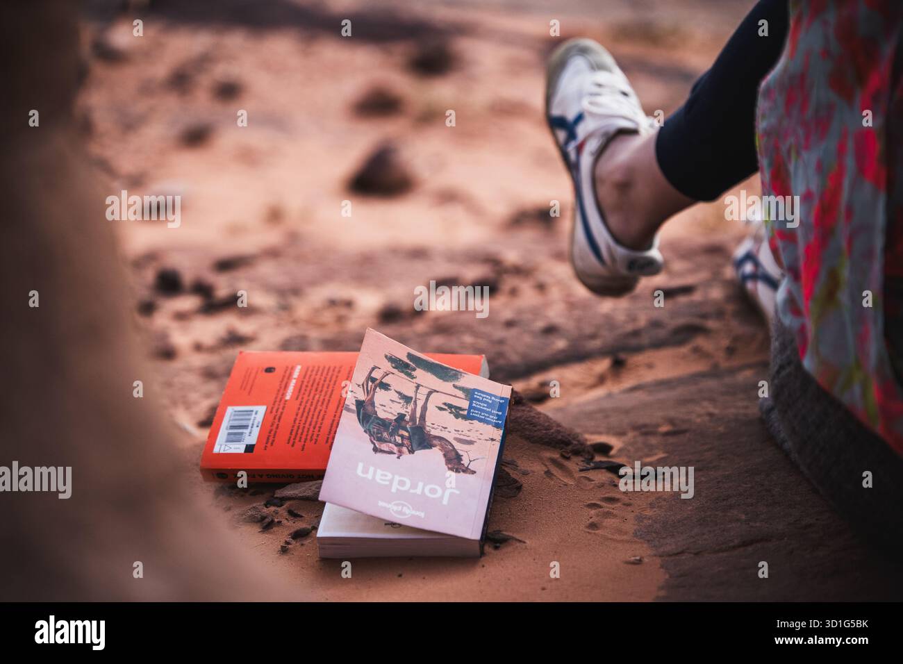 Jordan Reiseführer auf rotem Wüstensand neben Traveler’s Legs in Wadi Rum, Jordanien, 2024. Symbol für langsame Fahrt und Reflexion in der Wüste. Stockfoto