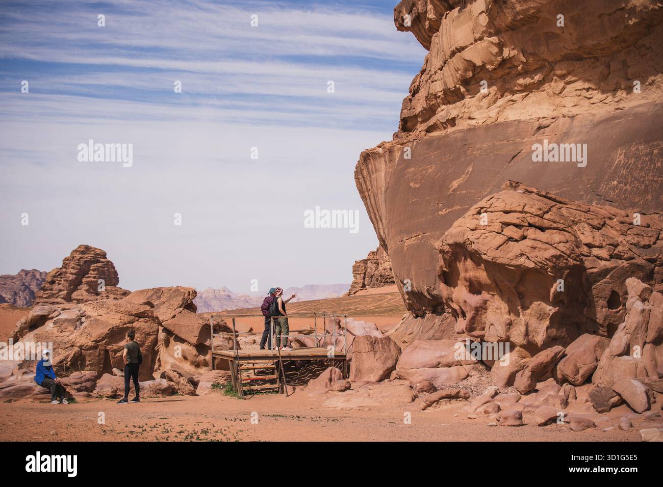 Touristen erkunden antike thamudische und nabatäische Petroglyphen, die in die Sandsteinklippen von Wadi Rum im Süden Jordaniens gehauen wurden. Stockfoto