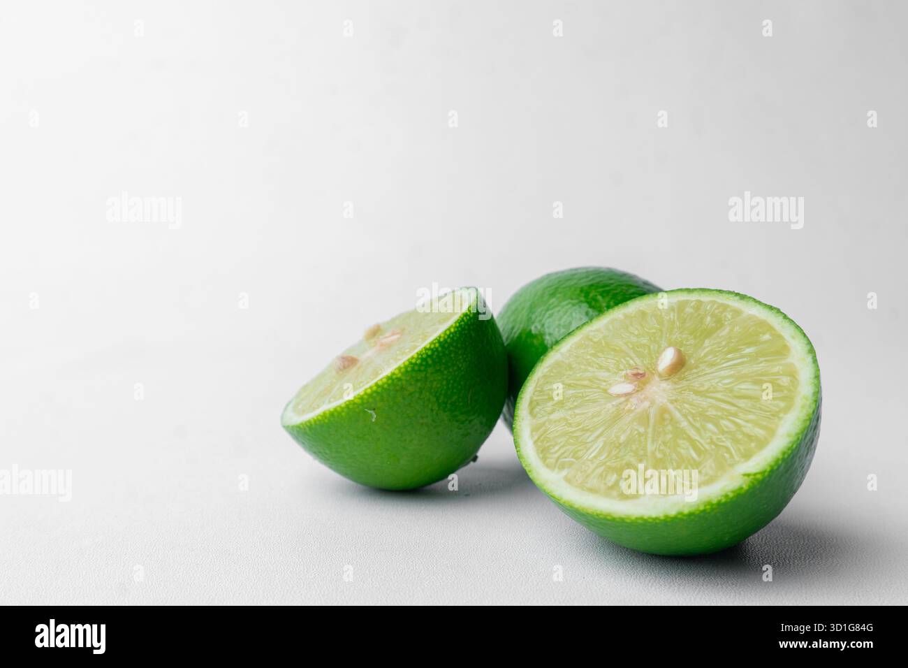 Frische grüne Limetten, ganz und in Hälften geschnitten. Isoliert auf einem sauberen weißen Hintergrund. Gesunde Zitrusfrüchte. Viel Kopierraum links. Stockfoto