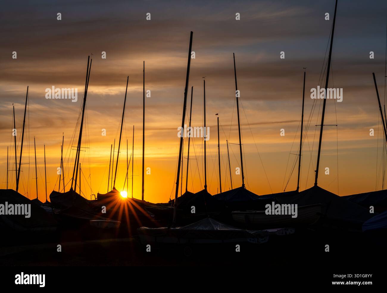 Sonnenaufgang zwischen verankerten Segelbooten und Masten an der Küste Stockfoto