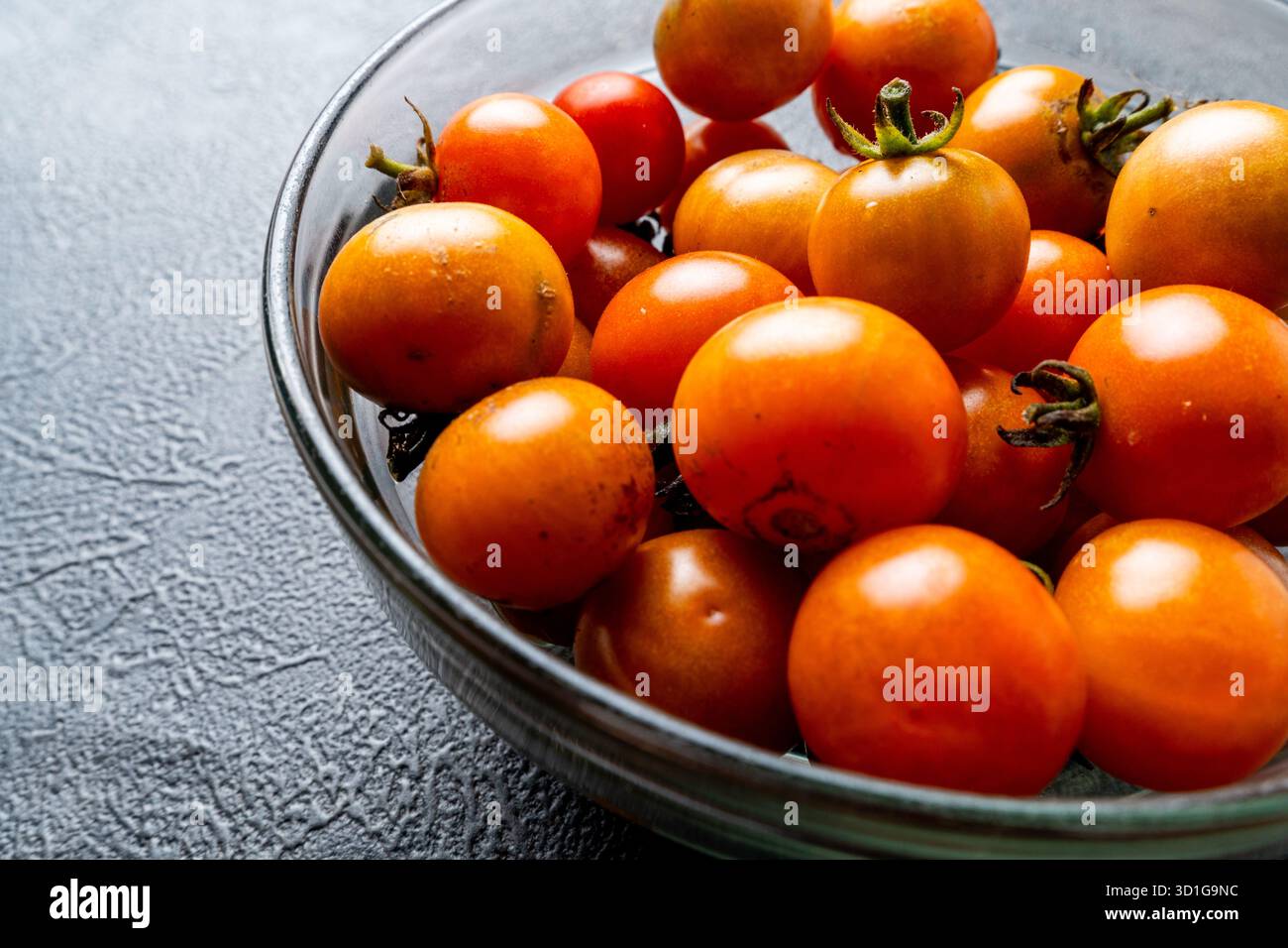 Eine Glasschale gefüllt mit frischen, Reifen Kirschtomaten auf einem dunklen, strukturierten Schieferhintergrund. Perfekt für gesunde Lebensmittelkonzepte, Rezepte, Stockfoto