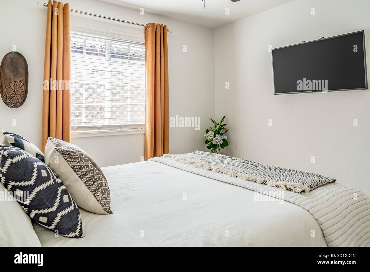 Modernes Schlafzimmer mit Inneneinrichtung in der Wüste mit Flachbildfernseher, Bett, Überwurf-Decke und Akzentkissen. Stockfoto