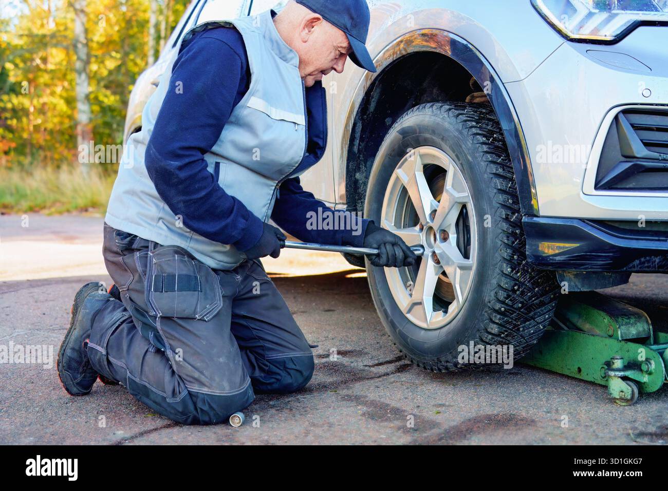 Der Kfz-Techniker kniet neben dem Fahrzeug, verwendet einen Schraubenschlüssel, um den Reifen am Straßenrand zu wechseln. Er demonstriert praktische Fähigkeiten und Engagement für Fahrzeug mai Stockfoto