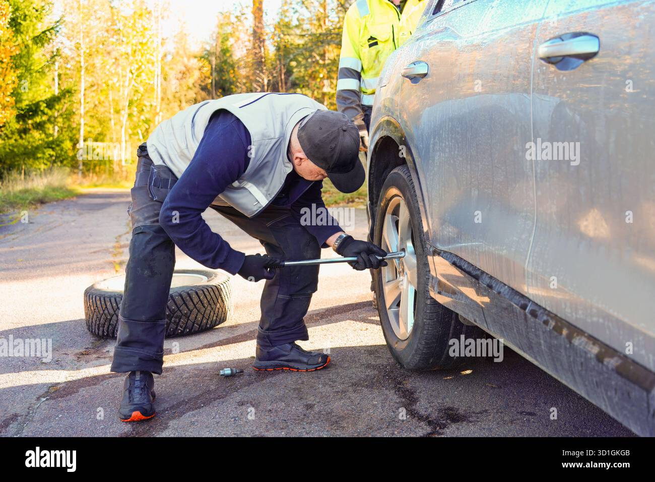 Ein Kfz-Techniker arbeitet am Reifenwechsel an einem Fahrzeug am Straßenrand und demonstriert praktische Fähigkeiten in einer ruhigen Umgebung im Freien Stockfoto