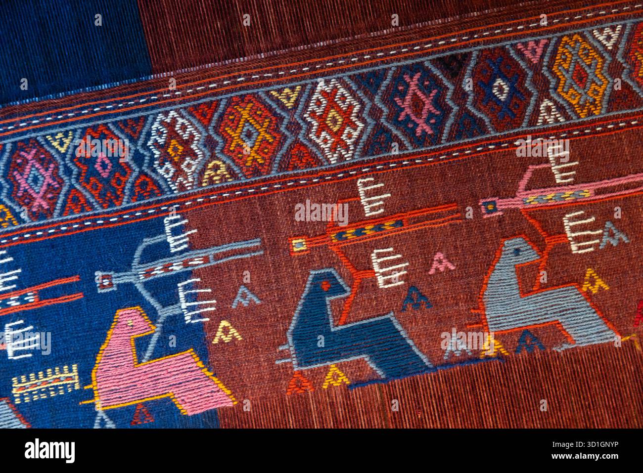 Lebendiger alter gewebter Teppich mit geometrischen Motiven, dekorativen Borten und abstrakten Tierfiguren in Rosa-, Blau-, Rot- und Brauntönen. Perfekt für TRA Stockfoto