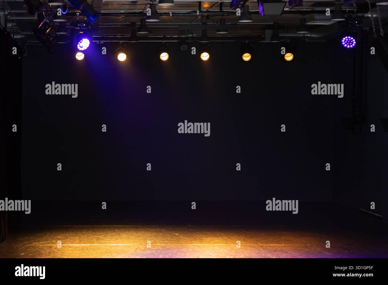 Eine leere Bühne mit dunklem Hintergrund und warmen Deckenleuchten. Violette Spots sorgen für eine stimmungsvolle, vorausschauende Stimmung, ideal für Aufführungen, Proben, Stockfoto