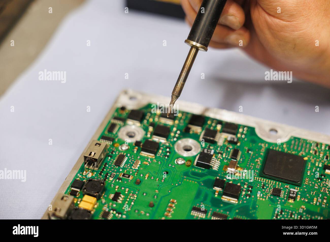 Eine Einzelperson lötet eine Hauptplatine mit einem Lötkolben sorgfältig und konzentriert sich dabei auf die präzise Platzierung elektronischer Bauteile Stockfoto