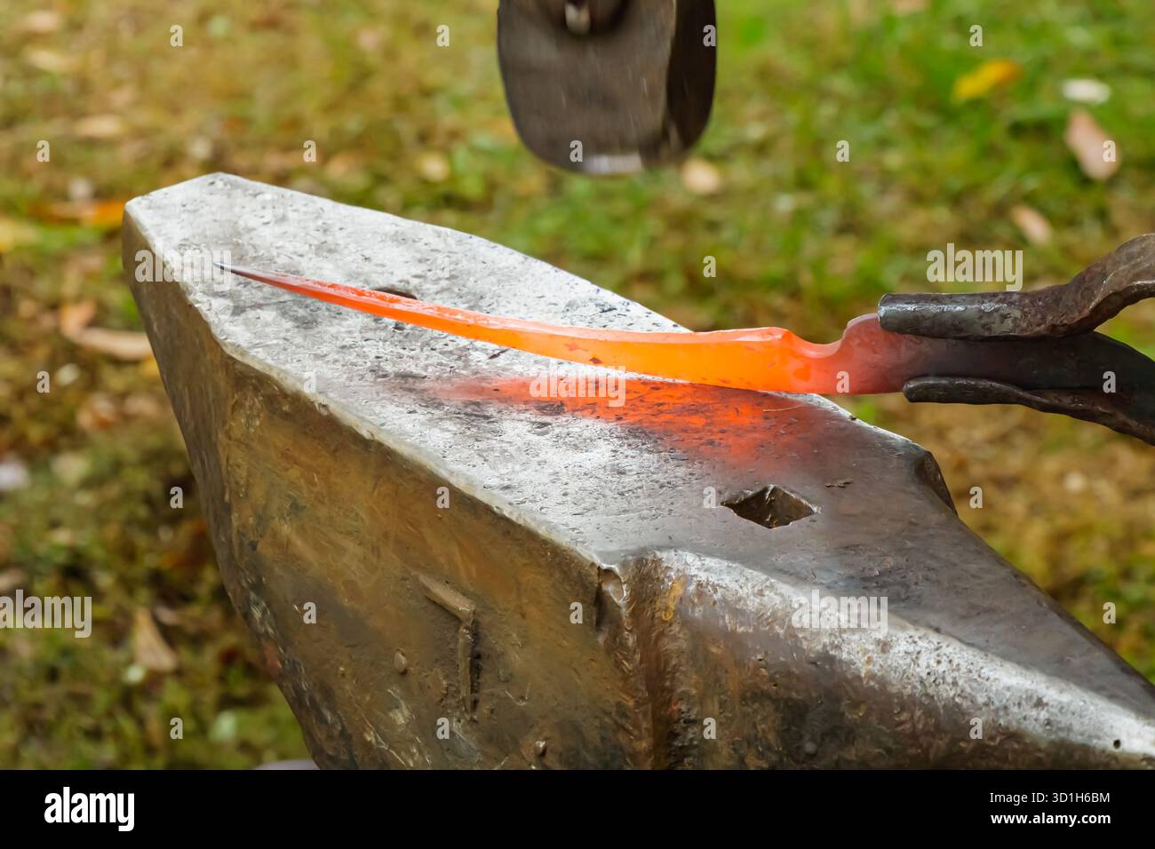 Nahaufnahme eines Schmieds, der an einem glühenden Stück heißes Metall mit Zange und Hammer über einem Amboss arbeitet. Das Foto hebt Handwerkskunst, Wärme und tr hervor Stockfoto
