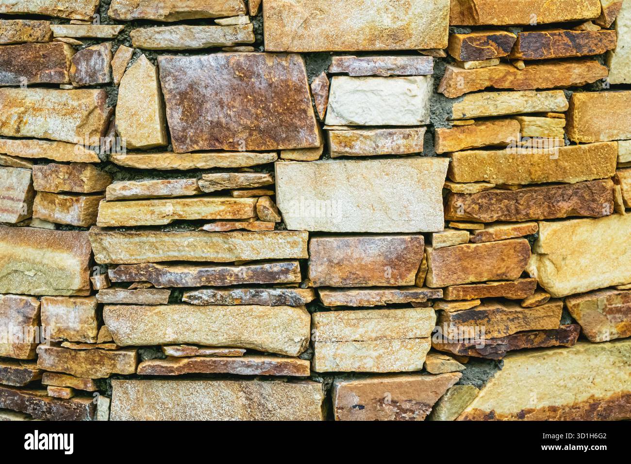 Nahaufnahme einer rustikalen Steinmauer aus unebenen Naturfelsen in Braun-, Beige- und Ockertönen. Die detaillierte Textur und die Erdfarben heben hervor Stockfoto