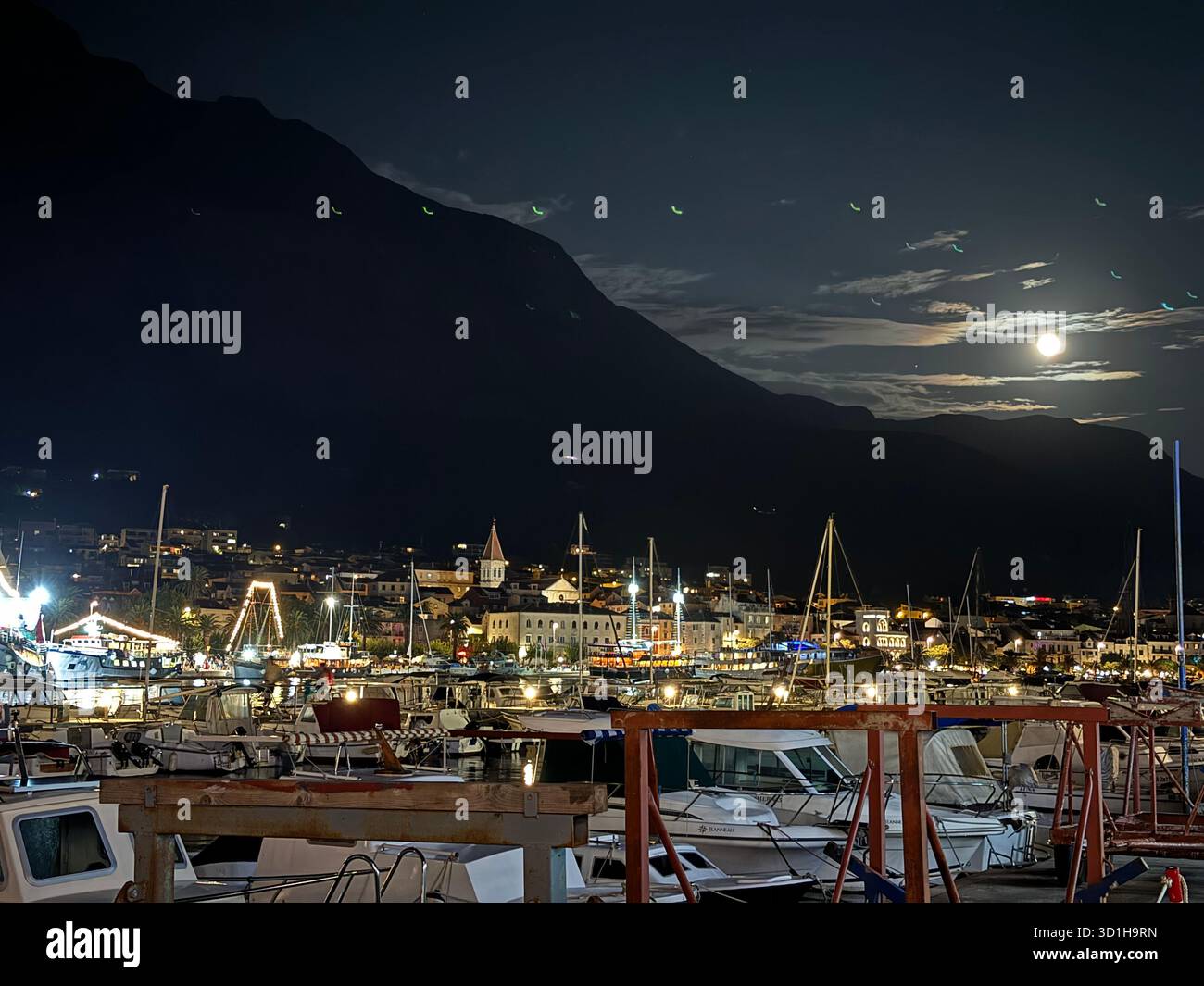 Pulsierende Nachtlandschaft eines Mittelmeerhafens mit Booten, Vollmond und Dark Mountain - Smartphone-aufgenommenes Stockfoto