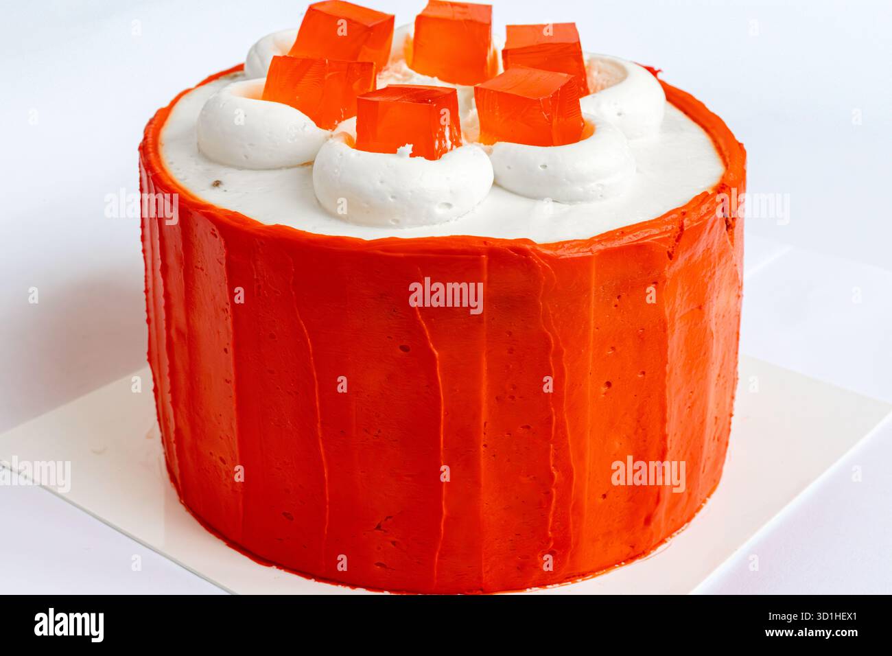 Leuchtend orange Torte mit cremigem Zuckerguss und farbenfrohen Gelatinequadraten, perfekt für festliche Feiern. Stockfoto