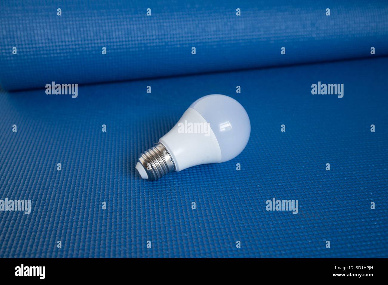 Energiesparende LED-Lampe auf strukturiertem blauem Hintergrund, die Effizienz und moderne Technologie repräsentiert. Stockfoto