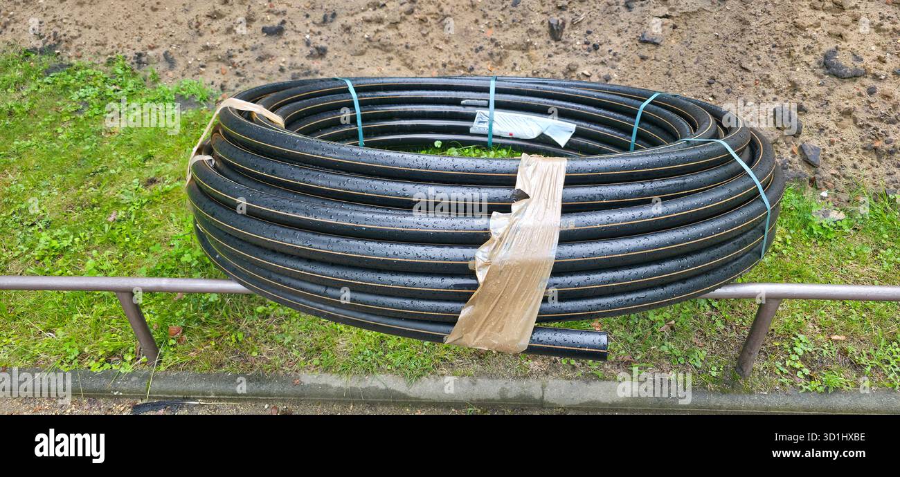 Schwarze Spiralrohre liegen auf einer grasbewachsenen Oberfläche, umgeben von natürlichen Elementen, die industrielle Materialien im Freien präsentieren. - Smartphone-aufgenommenes Stockfoto