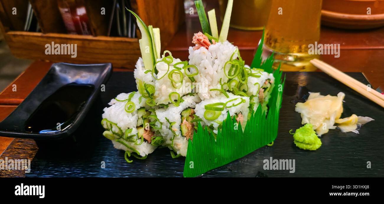 Frische Sushi-Brötchen werden wunderschön mit grünen Zwiebeln garniert und auf einem schwarzen Teller mit Wasabi und Ingwer serviert, was eine appetitliche Präsentation schafft. - Smartphone-aufgenommenes Stockfoto