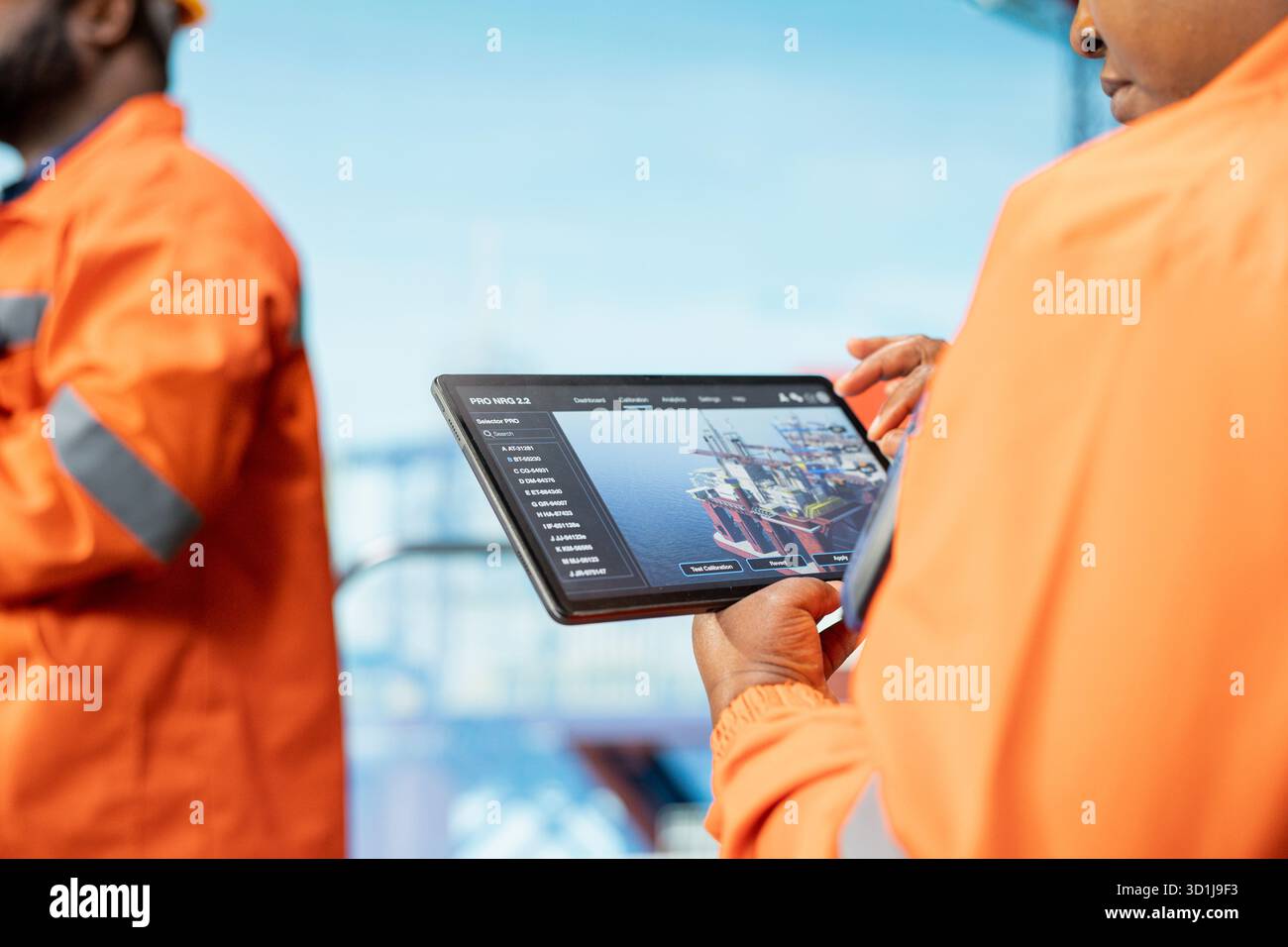 Nahaufnahme von Experten für Offshore-Plattformen, die die Leistung von Geräten in Echtzeit über eine Tablet-App überwachen. Bohrgerätekollegen arbeiten zusammen, um das Getriebe mit dem Asset Management System am Gerät zu kalibrieren Stockfoto
