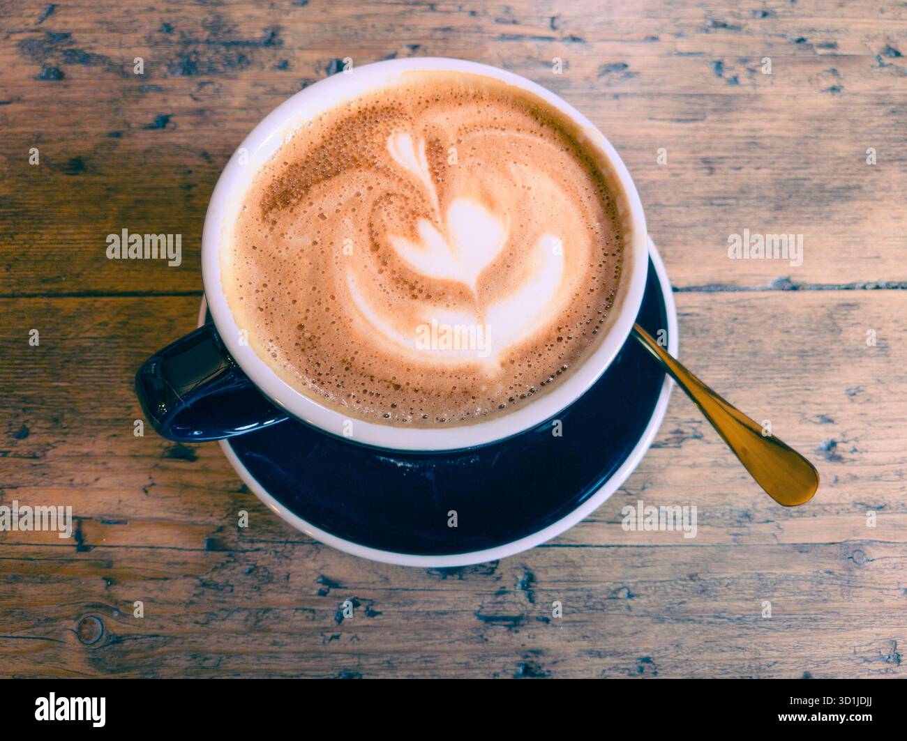 Flacher weißer Kaffee in einer Porzellantasse mit Blumenmuster aus geschäumter Milch (Mikroschaum), die in Espresso gegossen wird, auch bekannt als Latte Art Stockfoto