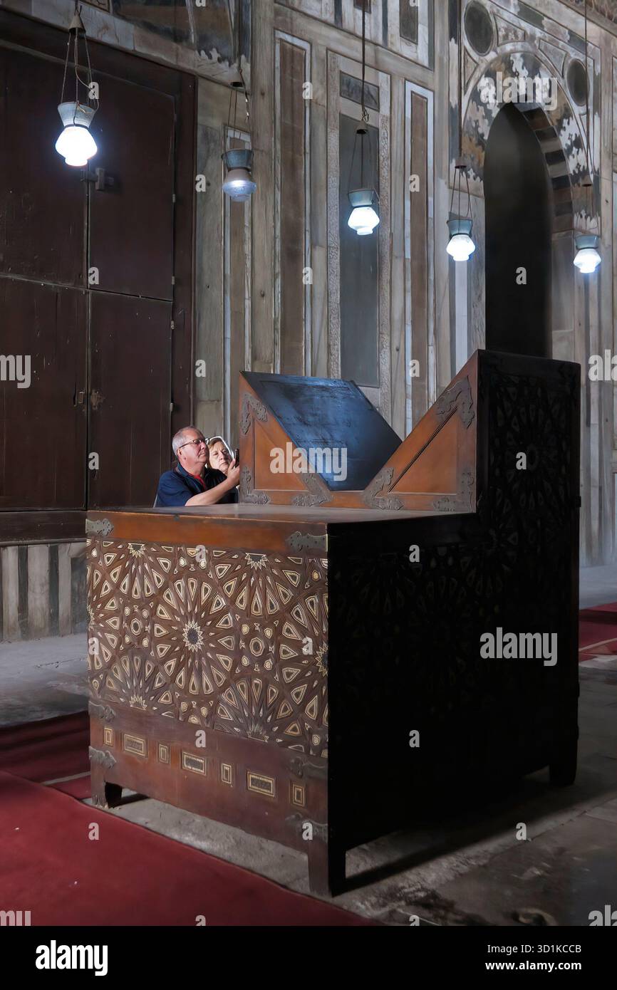 Touristen bewundern einen kunstvollen Koranhalter aus Holz in der Moschee-Madrasa von Sultan Hasan in Kairo, Ägypten Stockfoto